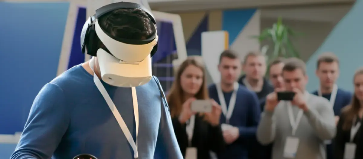 Visitante con visor de realidad virtual en un stand mientras el público lo filma